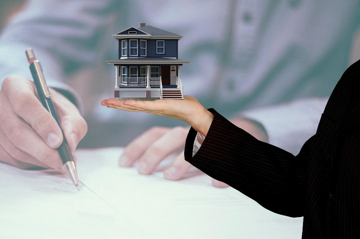 Une main tend un modèle de maison vers une autre main écrivant Une main tend un modèle de maison vers une autre main écrivant