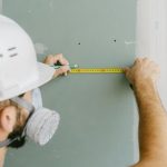 Un ouvrier en protection mesure un mur avec un ruban jaune