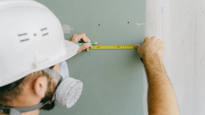 Un ouvrier en protection mesure un mur avec un ruban jaune