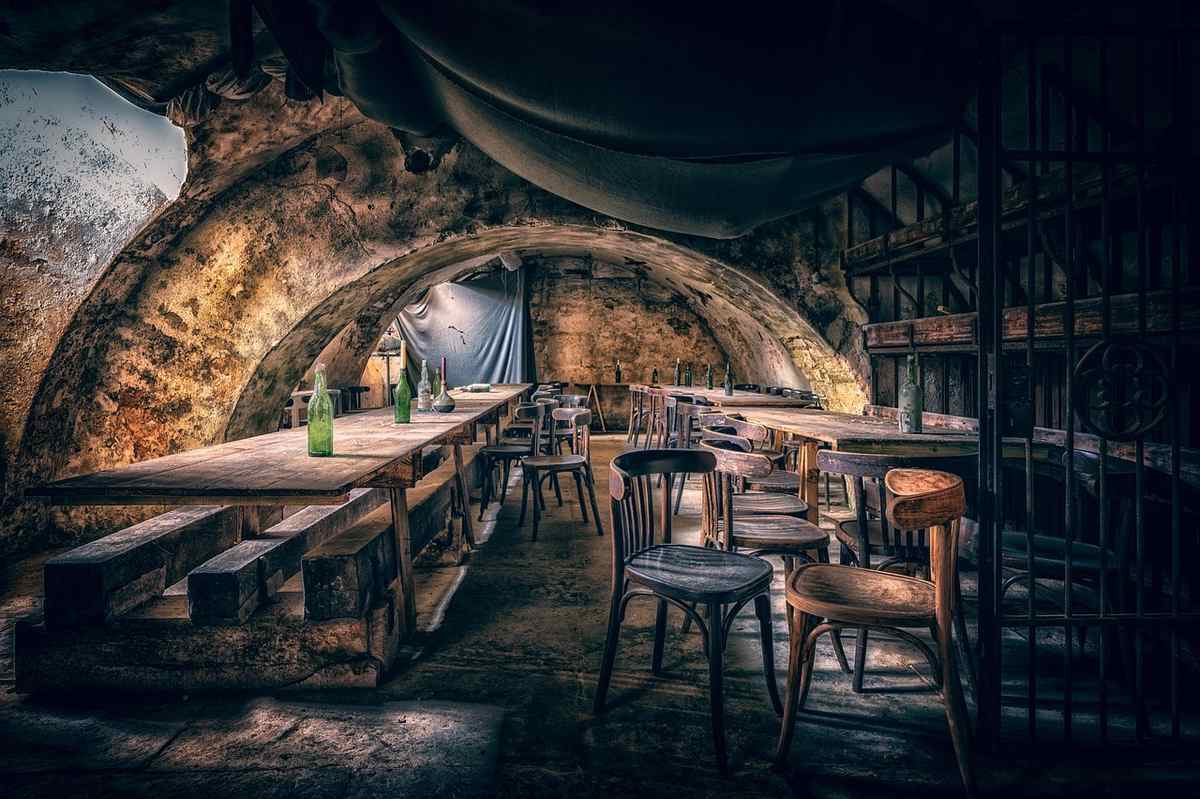 Une cave souterraine avec tables en bois, chaises et bouteilles, éclairée faiblement Une cave souterraine avec tables en bois, chaises et bouteilles, éclairée faiblement